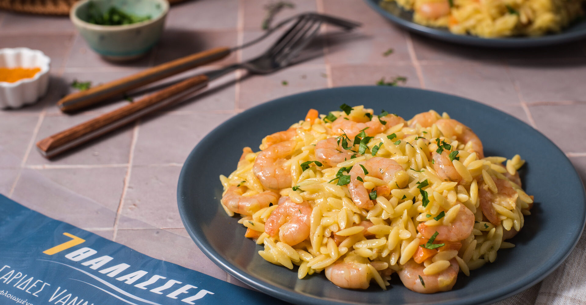 Κριθαρότο με γαρίδες σε μπλε πιάτο, σερβιρισμένο με μυρωδικά.